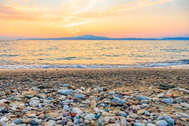 Kayalık bir kıyı şeridi ve arka planda güzel bir günbatımı olan bir sahil. Gökyüzü bulutlarla dolu ve su sakin. Sahne huzurlu ve huzurlu, kayalıklarla.