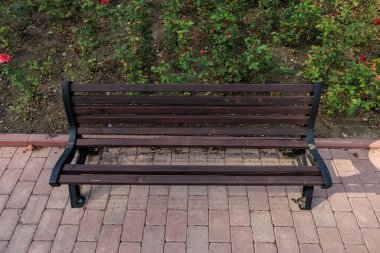 Tahta bir bank tuğla bir geçitte oturuyor. Yedek kulübesi boş ve yürüyüş yolu da boş, kırık bir element.