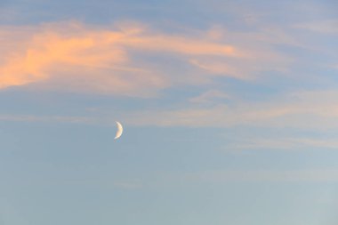 Hilal ve pastel bulutlar sakin bir gökyüzünde alacakaranlıkta.