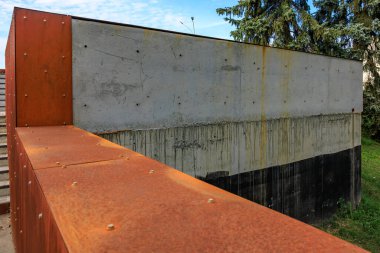 Paslı kahverengi boyalı ve siyah boyalı bir duvar. Duvar betondan yapılmış. Duvar bir parkta.