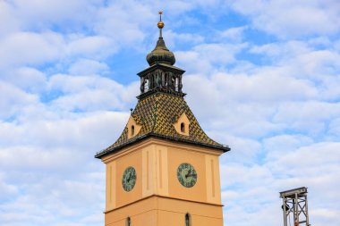 Çan kulesi ve her iki tarafında da saat olan uzun bir saat kulesi. Gökyüzü mavi ve bulutlu.