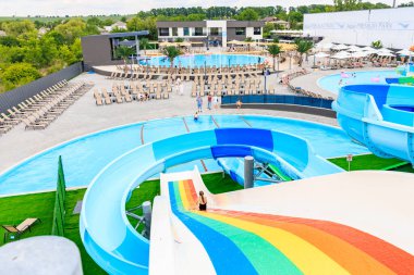 Üzerinde gökkuşağı olan renkli bir kaydırak bir su parkında. Kaydırak bir havuz ve birkaç sandalyeyle çevrili. 8 Haziran 2024 Balti Moldova
