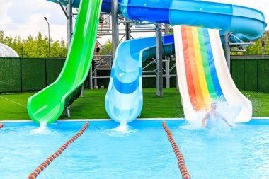 Bir insan havuzda gökkuşağı kaymasından kayıyor. Kaydırak yeşil, mavi ve beyaz. 8 Haziran 2024 Balti Moldova