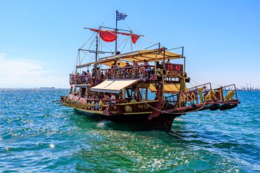 Kırmızı yelkenli ve beyaz tenteli büyük bir tekne okyanusta yüzüyor. Tekne insan kaynıyor ve teknede birkaç bayrak var. 8 Ağustos 2024 Selanik Yunanistan