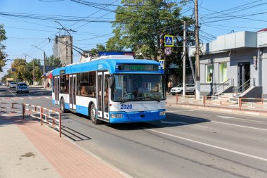 Arka planda ağaçlar ve binalar olan şehir caddesinde mavi ve beyaz bir troleybüs. 9 Eylül 2024 Balti Moldova.