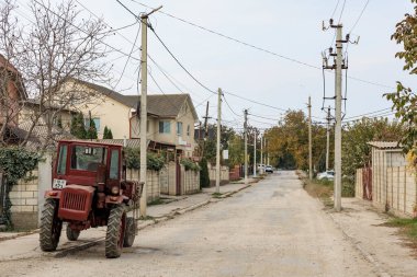 Sessiz mahalledeki toprak yolda kırmızı traktörlü kırsal sokak manzarası. 28 Ekim 2024 Balti, Moldova.