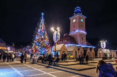 Kasaba meydanında bir Noel ağacı parlıyor. İnsanlar onun etrafında toplandı ve oturmaları için çeşitli bank ve sandalyeler var. Atmosfer neşeli ve şen şakrak. 13 Aralık 2024 Brasov Romanya