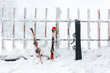 Karla kaplı kayaklar ve kar kayakları dağdaki buzlu ahşap çitlere karşı. 15 Aralık 2024 'te Romanya.