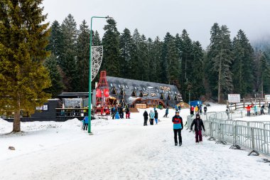 Turistlerin ve çam ormanı yakınlarındaki kır evlerinin olduğu karlı bir tatil köyünde kış aktiviteleri. 15 Aralık 2024 'te Romanya.