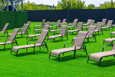 Bir sürü şezlonglu ve çitli büyük bir çimen. Bahçe sandalyeleri boş ve çimenler yeşil.