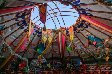 Ortasında büyük bir delik olan renkli bir çadır. Çadır, Kırgız otantik göçebe yurdundaki bir çok renkli bayrak ve bayrakla süslenmiştir.