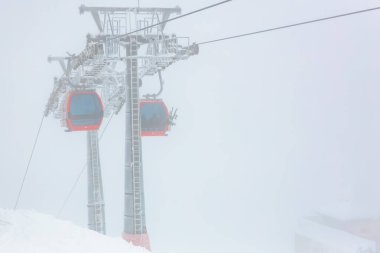 Kış karları boyunca puslu dağ manzarasında kırmızı teleferikler..