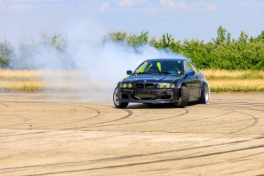Modifiye edilmiş siyah bir BMW, açık bir pistte dönerken yoğun bir duman izi bırakarak sürükleniyor. 2 Temmuz 2023 Liadoveni Moldova.
