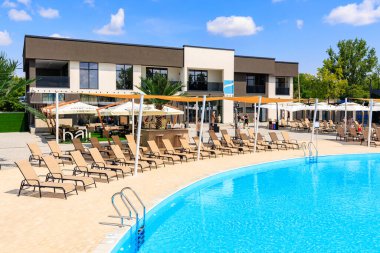 Birçok şezlonga ve şemsiyeye sahip büyük bir havuz kumlu bir alanla çevrilidir. Sandalyeler havuzun etrafında daire şeklinde dizilir, suya yakın sandalyeler ve daha uzak sandalyeler. 8 Haziran 2024 Balti Moldova