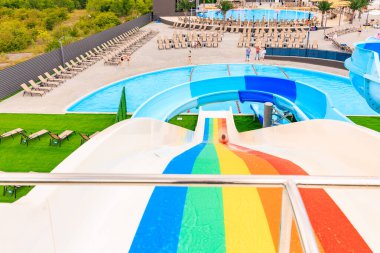 Üzerinde gökkuşağı olan renkli bir kaydırak bir su parkında. Kaydırak sandalyeler ve diğer dinlenme odaları ile çevrilidir. 8 Haziran 2024 Balti Moldova