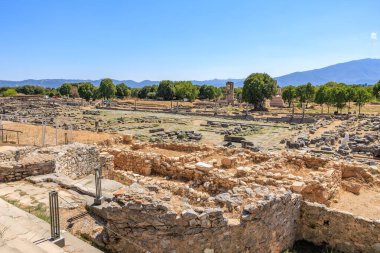 Birkaç ağaç ve birkaç bina olan geniş, açık bir alan. Binalar eski ve harabe gibi görünüyor. Gökyüzü açık ve güneş ışıl ışıl parlıyor. Yunanistan 'ın antik Filippi kentinin kalıntıları