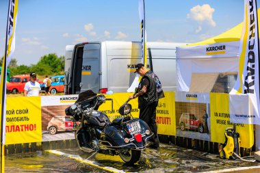 Bir motorcu, motosikletini dışarıdaki temizlik kabininde temizlemek için güçlü bir basınç makinası kullanır. Etkili araç temizleme ürünleri gösteriliyor. 2 Temmuz 2023 Liadoveni Moldova.