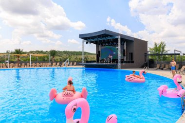 Bir grup insan havuzda şişirilebilir pembe flamingo şekilli sallarda yüzüyorlar. Sahne canlı ve eğlenceli, insanlar eğleniyor. 8 Haziran 2024 Balti Moldova