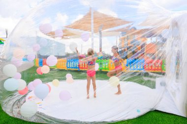 İki genç kız açık bir balonda balonlarla oynuyorlar. Kabarcık çeşitli renk ve boyutlarda balonlarla dolu, eğlenceli ve eğlenceli bir atmosfer yaratıyor. 8 Haziran 2024 Balti Moldova
