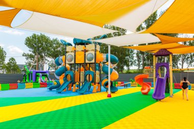 Üzerinde sarı ve beyaz bir gölgelik olan bir oyun alanı. Slayt, salıncak ve tırmanma da dahil olmak üzere birçok farklı oyun alanı ekipmanı vardır. Bir kadın oyun alanının yanından geçiyor. 8 Haziran 2024 Balti Moldova