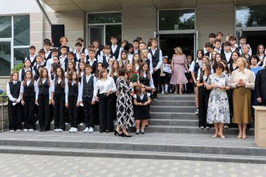 Bir grup üniformalı öğrenci okul merdivenlerinde öğretmenlerle toplanıyor. 2 Eylül 2024 Balti Moldova.