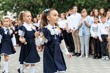 Üniformalı beyaz kızlar okul töreninde yetişkinler ve çocuklar izlerken zil çalıyorlar. 2 Eylül 2024 Balti Moldova.