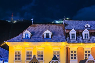 Üzerinde yeşil işaret olan sarı bir bina. Bina gece aydınlanıyor.