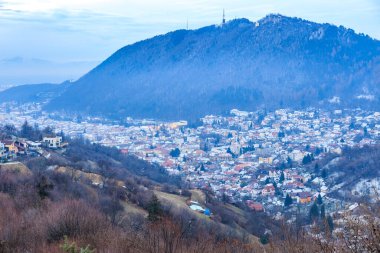 Arkasında dağ olan bir şehir. Şehir karla kaplı. Dağ da karla kaplı.