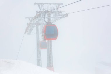 Sisli dağ manzarasında, karla kaplı yamaçlı kırmızı teleferikler..