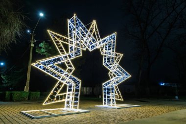 Gece vakti parkta aydınlatılmış geometrik yıldız heykeli.