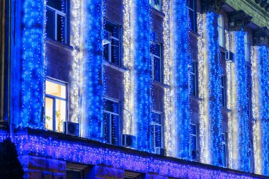 Gece vakti mavi ve beyaz tatil ışıklarıyla ön cephe inşa etmek. 20 Aralık 2024 Balti Moldova.