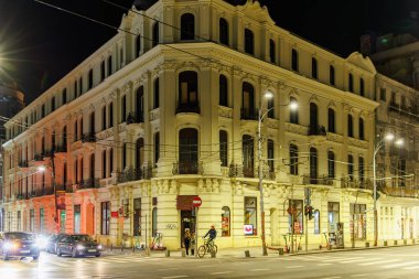 Şehrin işlek caddelerinin köşesindeki tarihi binanın gece manzarası. 8 Mart 2025 Bükreş Romanya.
