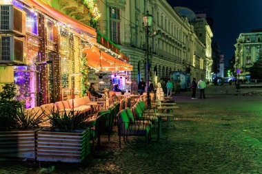 Aydınlatılmış bir kafesi ve kaldırım taşı yolu olan büyüleyici bir gece sokağı. 8 Mart 2025 Bükreş Romanya.