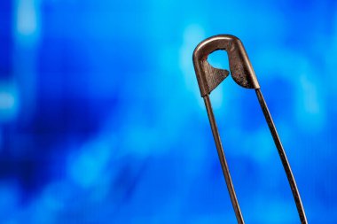 Güvenlik iğnesinin mavi soyut arkaplana yakın plan görüntüsü.