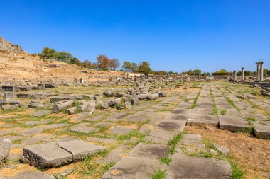 Üzerinde mavi bir gökyüzü olan geniş bir açık alan. Alan büyük taşlarla dolu ve ortasında çimenlik bir alan var. Yunanistan 'ın antik Filippi kentinin kalıntıları