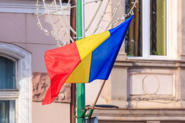Bir direğe asılı kırmızı, sarı ve mavi bayrak. Bayrak bir sokak köşesinde ve arkasındaki bina Romanya devletinin beyaz bayrağı.