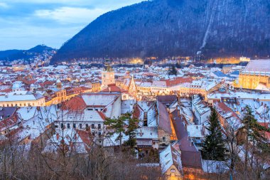 Geceleri binaların çatısında kar olan bir şehir. Şehir ışıklarla aydınlanıyor ve kar huzur dolu ve sakin bir atmosfer ekliyor.
