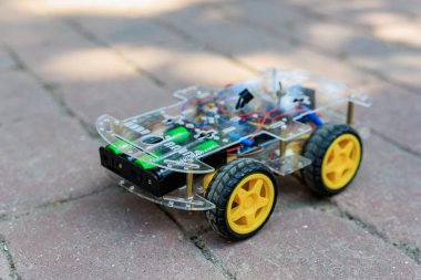 Küçük robot tuğla kaldırımda oturuyor. Robot plastikten yapılmış ve sarı bir tekerleği var.