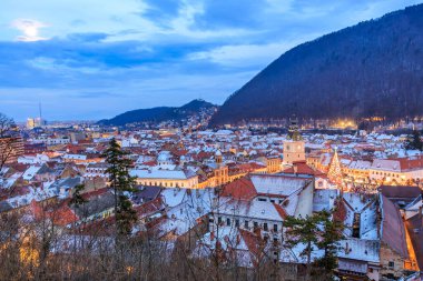 Gökyüzünde dolunay olan bir şehir. Şehir karla kaplı ve binalar aydınlık. 14 Aralık 2024 Brasov Romanya