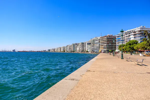 Mavi okyanusu ve binaları olan bir sahil. Binalar yüksek ve balkonları var. Sahil insanlarla dolu ve oturabilecekleri banklar var. 8 Ağustos 2024 Selanik Yunanistan