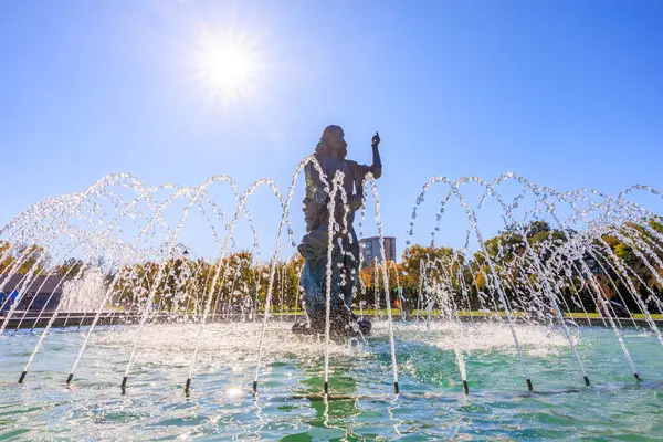 Bir insan heykeli çeşmenin önünde duruyor. Çeşme havaya su püskürtüyor. Güneş ışıl ışıl parlıyor, sahneyi parlak ve neşeli gösteriyor. 27 Ekim 2024 Chisinau Moldova