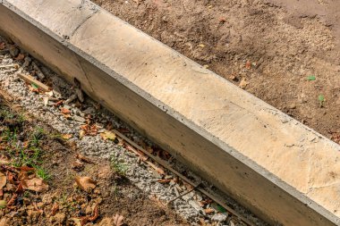 Etrafında bir sürü enkaz ve kir olan beton bir kaldırım görülüyor. Kaldırım çimenli bir alandadır ve üzerinde bir sürü yaprak ve dal vardır.