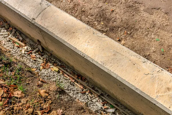 Etrafında bir sürü enkaz ve kir olan beton bir kaldırım görülüyor. Kaldırım çimenli bir alandadır ve üzerinde bir sürü yaprak ve dal vardır.