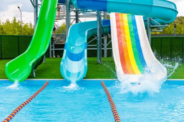 Üç slaytlı bir havuz, biri yeşil, biri mavi ve biri beyaz. Yeşil slayt havuzun ortasında, ve mavi ve beyaz slaytlar da iki tarafında. Havuz suyla dolu.