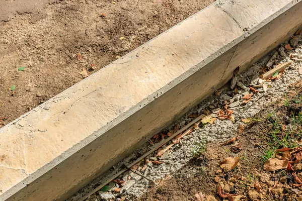 Toprak bir yolda beton bir kaldırım inşa ediliyor. Kaldırım betondan yapılmış ve kırsal bir alanda inşa ediliyor. İnşaat işçileri beton döşemek için kürek ve diğer aletleri kullanıyorlar.