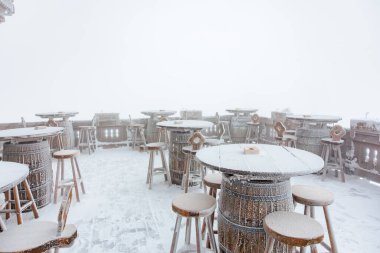 Boş ahşap masaları ve kışın sisli sandalyeleri olan karla kaplı bir avlu..