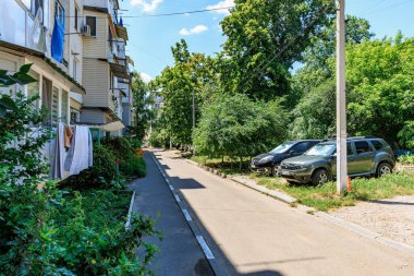 Bereketli bir yeşillik ve güneşli bir günde park edilmiş arabalarla banliyö caddesi manzarası. 12 Haziran 2024 Balti Moldova.