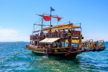 Kırmızı yelkenli ve beyaz tenteli büyük bir tekne okyanusta yüzüyor. Tekne insan kaynıyor ve teknede birkaç bayrak var. 8 Ağustos 2024 Selanik Yunanistan