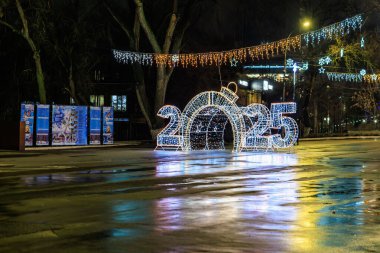 Gece ıslak sokağa yansıyan şenlik ışıklarıyla 2025 tabelasını yaktı. 27 Aralık 2024 Balti Moldova.