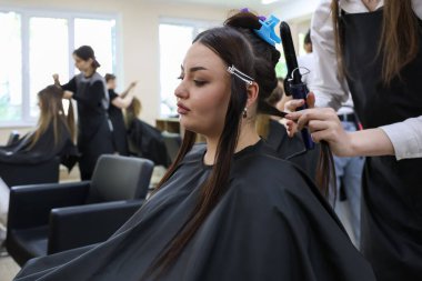 Asyalı kadın kuaför salonunda saç maşasıyla tedavi görüyor. 30 Nisan 2024 Balti Moldova.